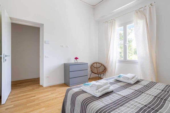 Une chambre à coucher avec un lit, une commode, une chaise et une fenêtre avec des rideaux.