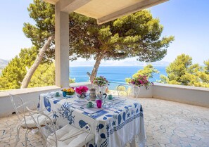 Een terras met een eettafel, met uitzicht op een schilderachtig zee- en boslandschap.
