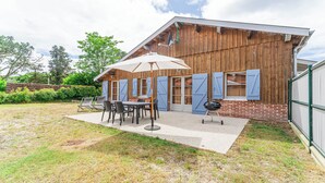 En rustik træbygning med en patio, der har et bord, stole, grill og stor parasol.