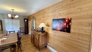 Een eetgedeelte met een houten tafel, stoelen en een kast. Op de muur hangt een klok en een spiegel.