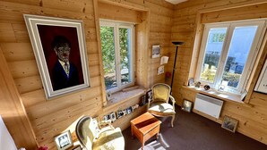 Een knus vakantiehuisje met houten wanden, een groot raam, een stoel, een kleine tafel en een lijst met een afbeelding aan de muur.