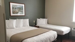 Una habitación de hotel con una cama grande, una cama más pequeña, una mesita de noche, un cuadro enmarcado en la pared y una ventana.