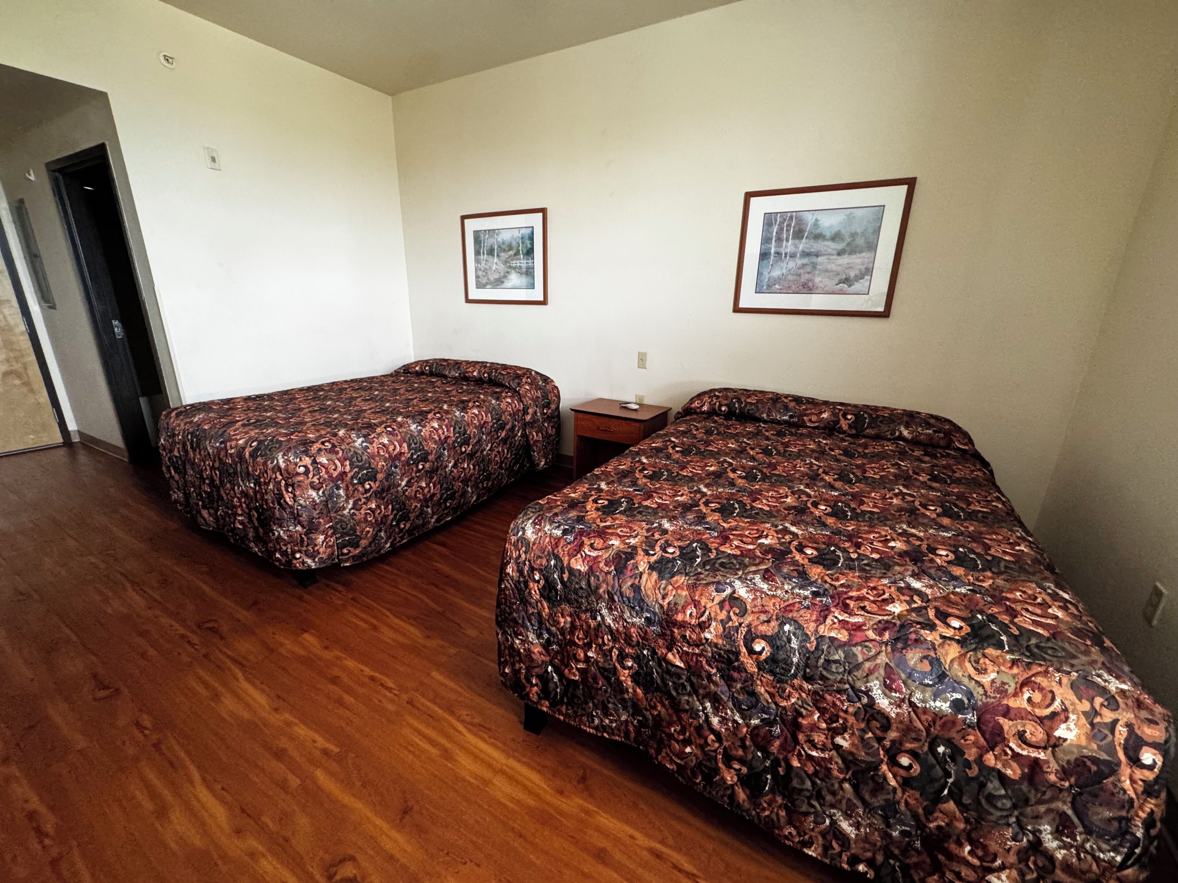 Habitació amb dos llits, un terra de fusta i dos quadres penjats a la paret.