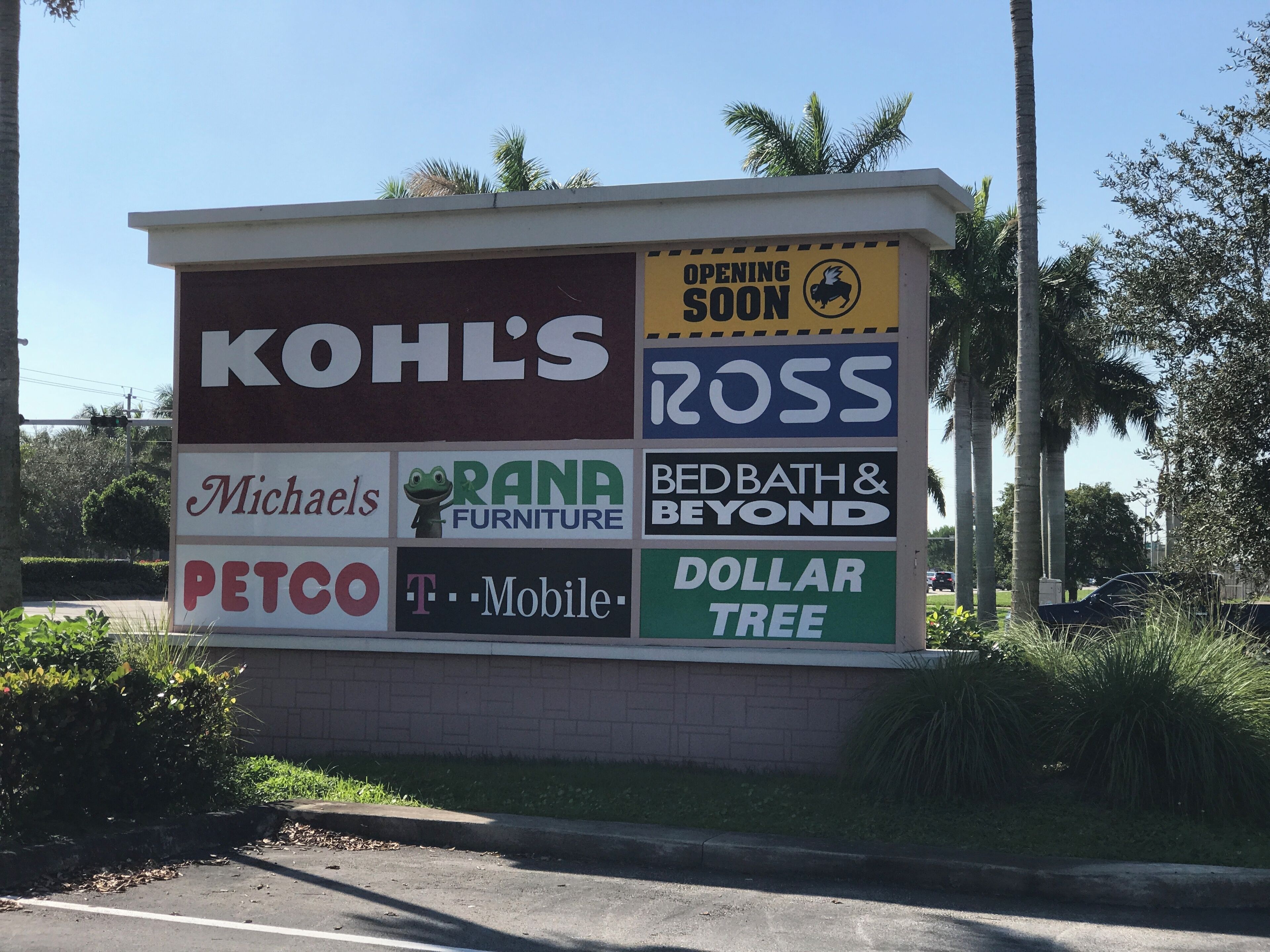 Suuri mainoskyltti, jossa on useita eri yritysten mainoksia, kuten KOHL'S, Ross, Michaels, RANA FURNITURE, BEDBATH & BEYOND, PETCO, T-Mobile ja DOLLAR TREE.