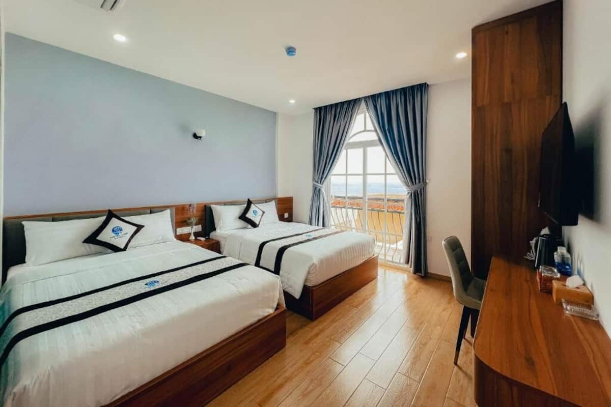 Une chambre d’hôtel avec deux lits, un bureau en bois, une télévision et un balcon avec vue.