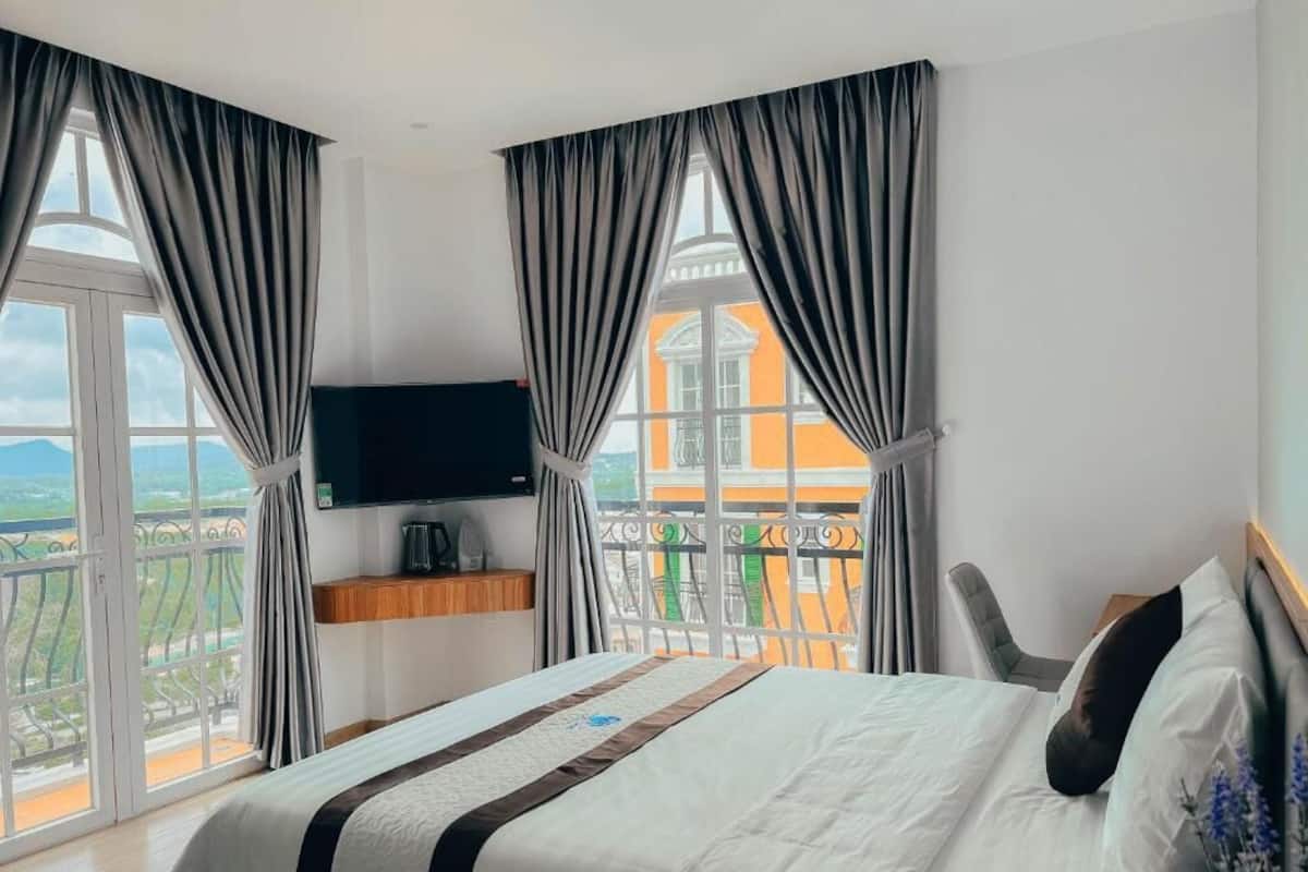 Une chambre d’hôtel avec un lit, une télévision, un balcon avec vue et des rideaux.