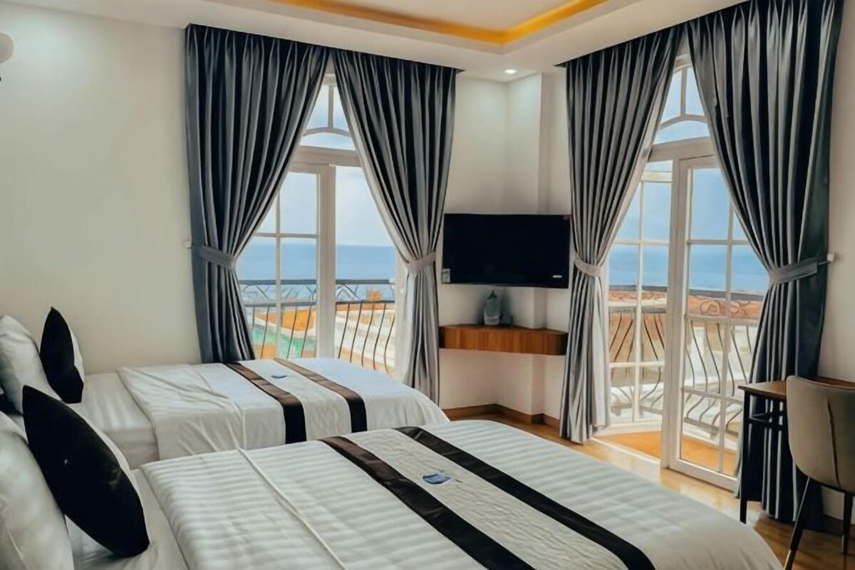 Een hotelkamer met twee bedden, een televisie en een balkon met uitzicht op zee.