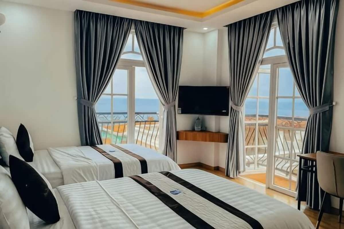 Une chambre d’hôtel avec deux lits, une télévision et un balcon donnant sur la mer.