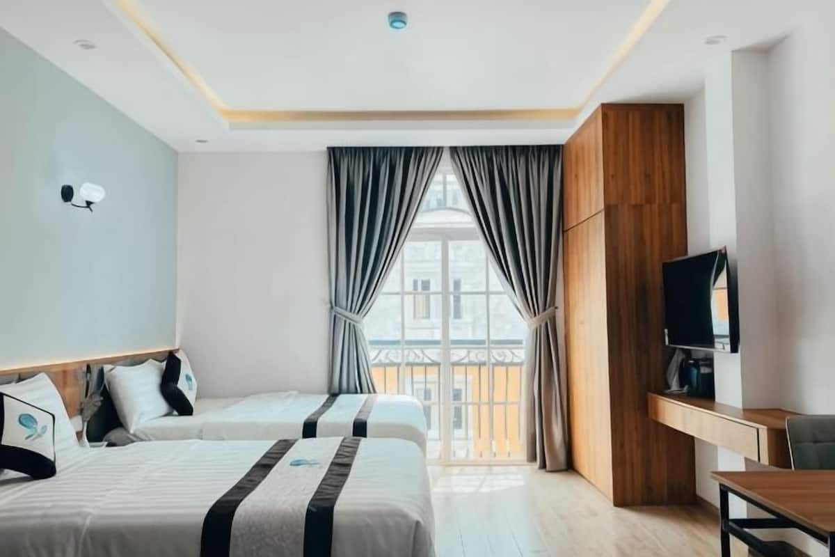 Une chambre d’hôtel avec deux lits, un bureau, une télévision et une fenêtre avec des rideaux.