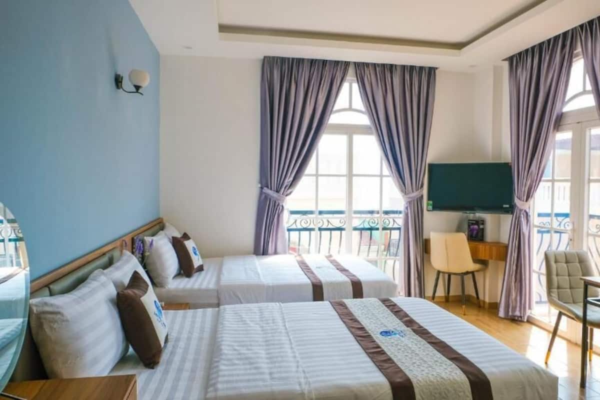 Une chambre d’hôtel avec deux lits, un bureau, une chaise et un balcon doté d’une rambarde.