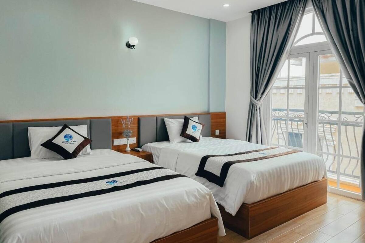 Une chambre d’hôtel avec deux lits, une table de chevet, une lampe fixée au mur et un balcon avec des rideaux.