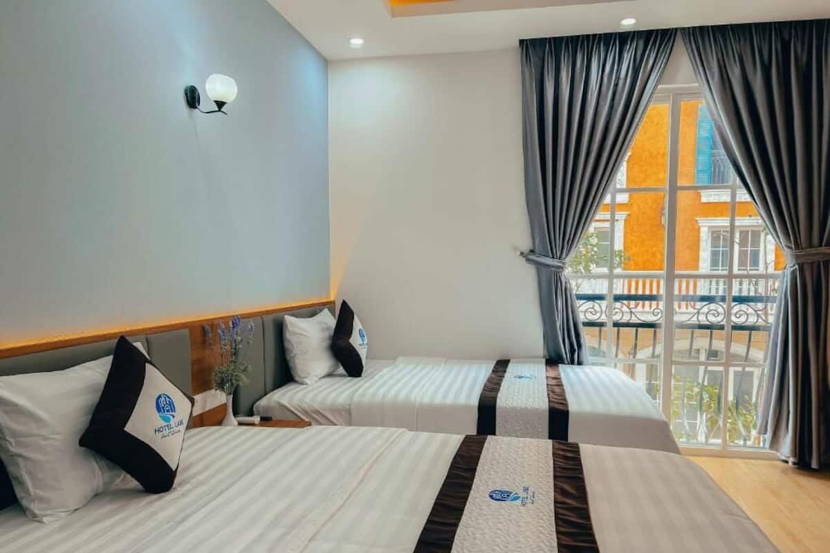 Une chambre d’hôtel avec deux lits, une table de chevet, une lampe fixée au mur et un balcon avec des rideaux.