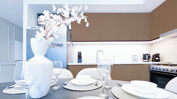 A modern dining area with a table set for four, including wine glasses, plates, and cutlery. - 2B With Stunning Burj Views at Burj Crown (Dubai)