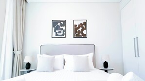 A neatly made bed with white linens and pillows, two bedside tables with lamps, and two abstract art pieces on the wall. - 2B With Stunning Burj Views at Burj Crown (Dubai)