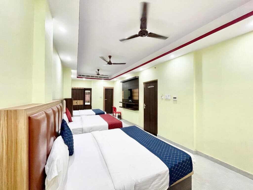 A hotel room with three beds, a wooden headboard, ceiling fans, and a television on the wall.