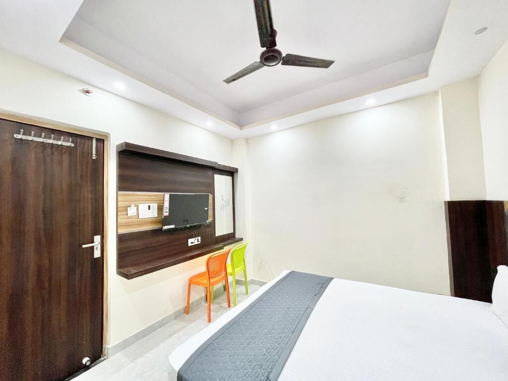 A hotel room with a bed, a desk with a computer, a chair, a wardrobe, and a ceiling fan.