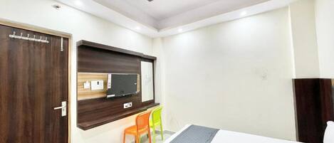 A hotel room with a bed, a desk with a computer, a chair, a wardrobe, and a ceiling fan.
