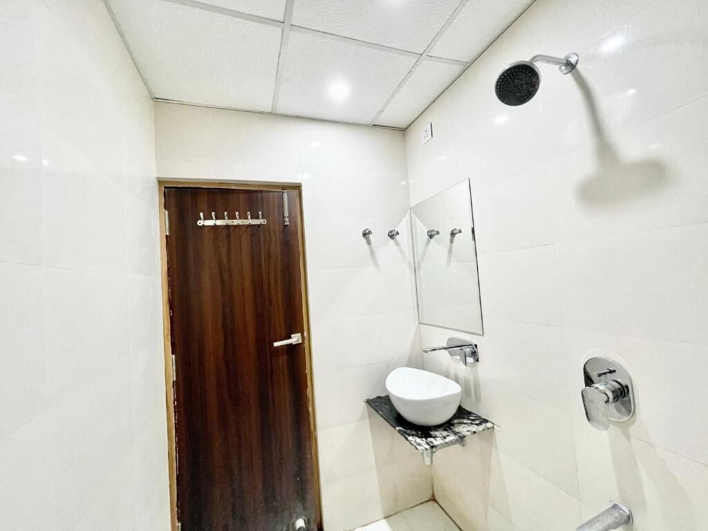 Une salle de bain avec une porte en bois, un lavabo blanc posé sur un plan de travail noir, un miroir et une douche équipée d’un pommeau de douche à main.