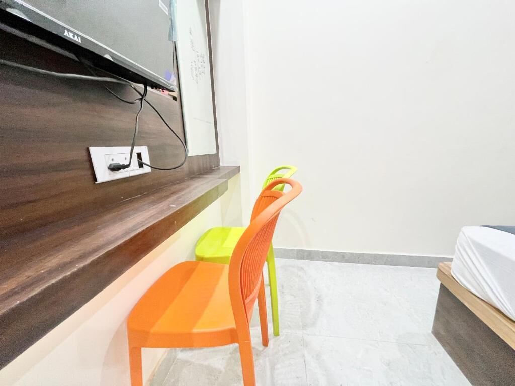 A room with a bed, a desk with a chair, a TV mounted on the wall, and a power outlet.