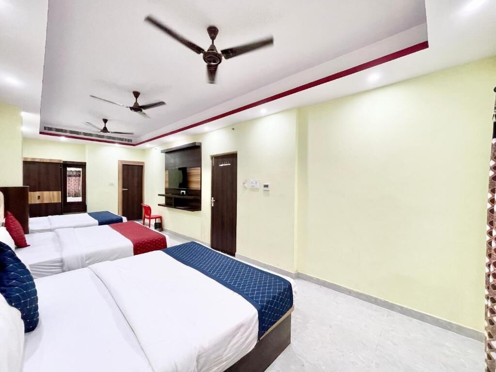 A hotel room with three beds, ceiling fans, a TV, and a red chair.