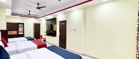 A hotel room with three beds, ceiling fans, a TV, and a red chair.