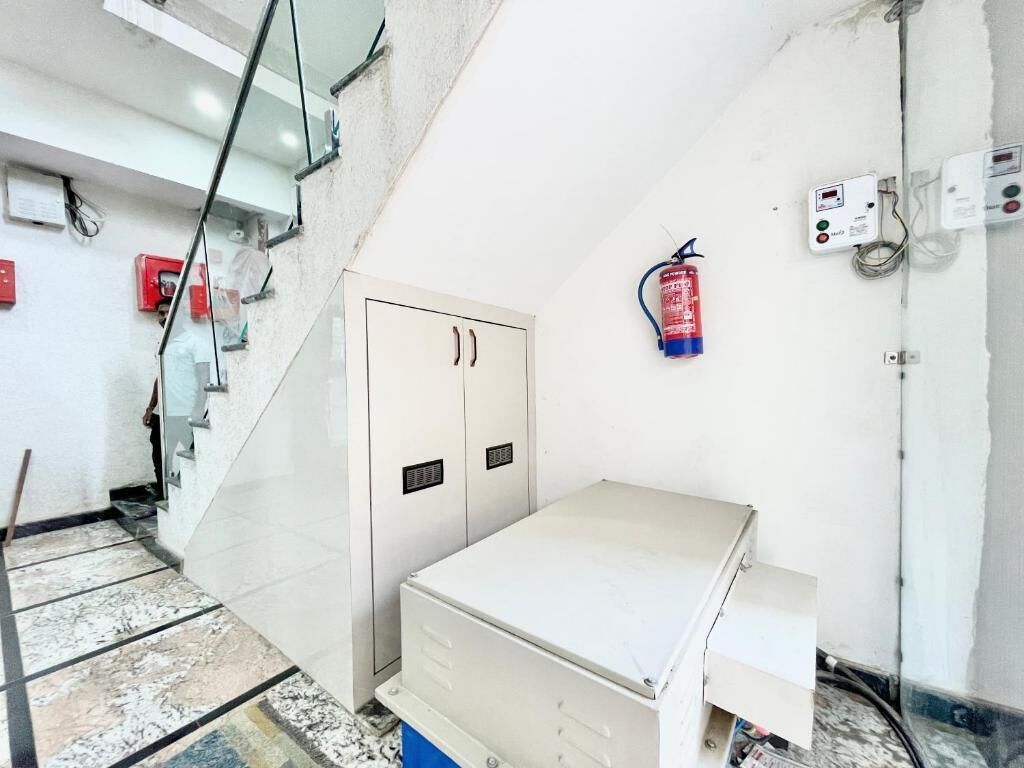 A room with a white cabinet, a fire extinguisher, and a control panel on the wall.