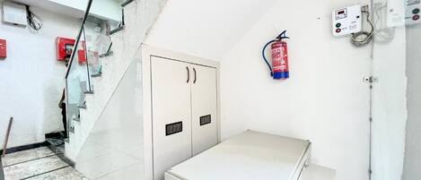 A room with a white cabinet, a fire extinguisher, and a control panel on the wall.