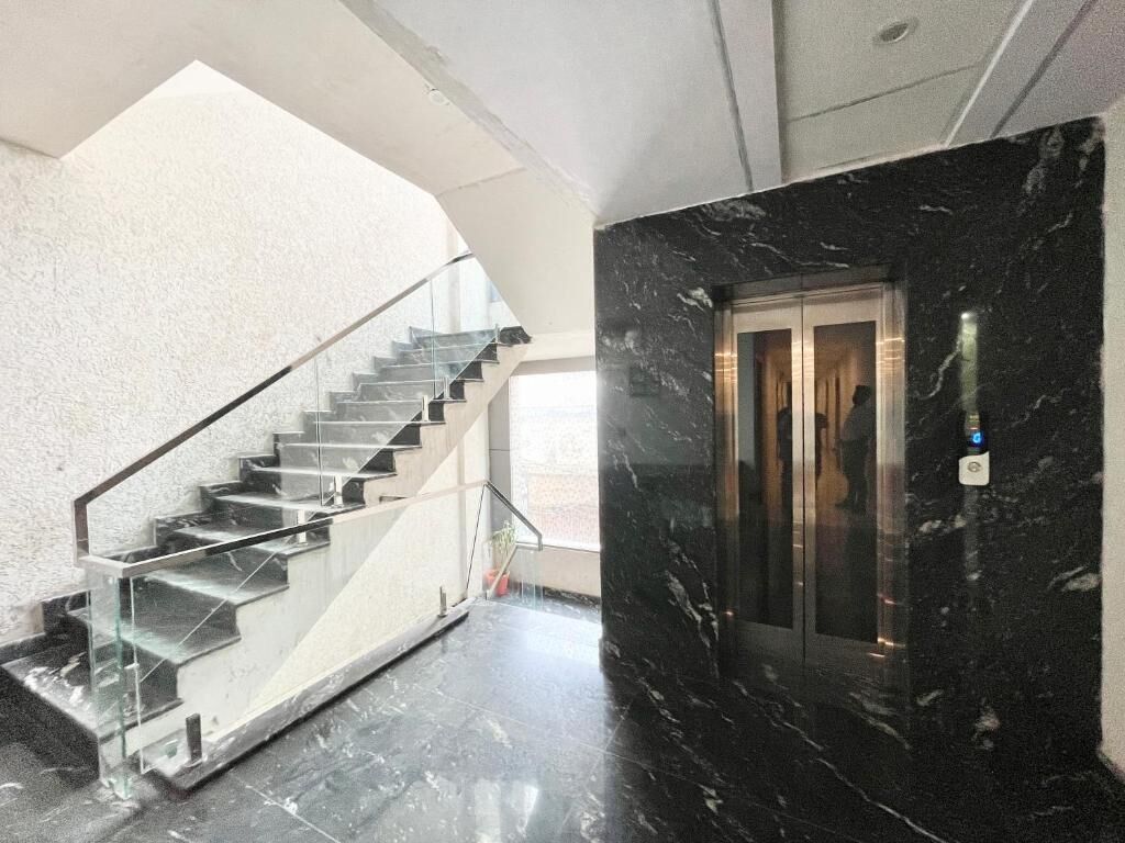 Un interior moderno con una escalera de cristal, una pared de mármol y un ascensor.
