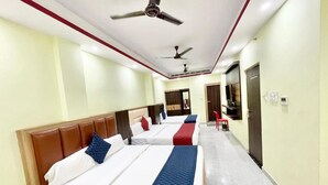 A hotel room with two beds, a ceiling fan, a TV, and a red chair. - Hotel LV Palace - near Ghats & Temples (Varanasi)