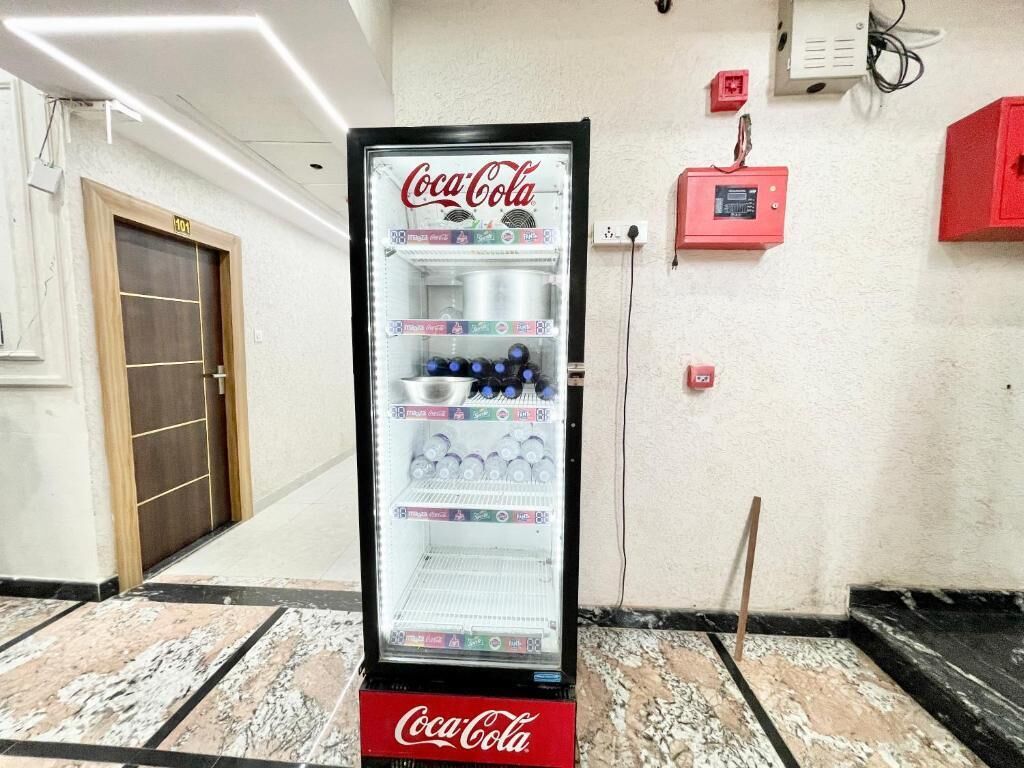 A Coca-Cola refrigerator in a hotel lobby with a wooden door and tiled floor.
