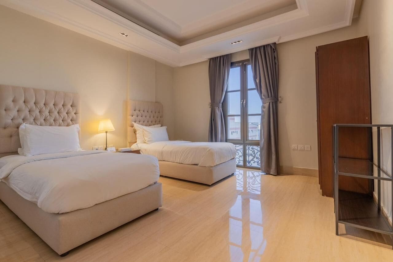 A hotel room with two beds, a large window with curtains, and a wooden wardrobe.