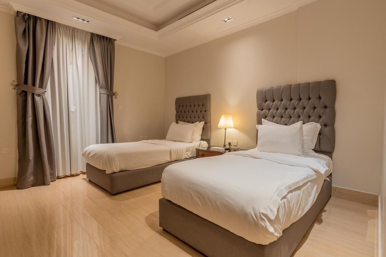 Una habitación de hotel con dos camas, un ventanal con cortinas y una lámpara en el techo.