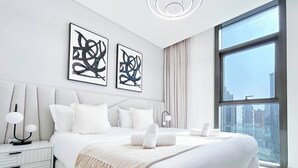 A modern bedroom with a large bed, two bedside tables, a large window with a city view, and abstract art on the wall.