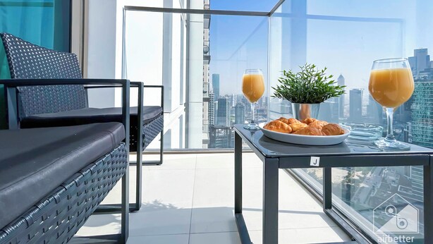 A balcony with a sofa, a table with a potted plant, two glasses of orange juice, and a plate of croissants.