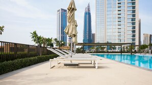 A poolside area with lounge chairs and umbrellas, surrounded by high-rise buildings.