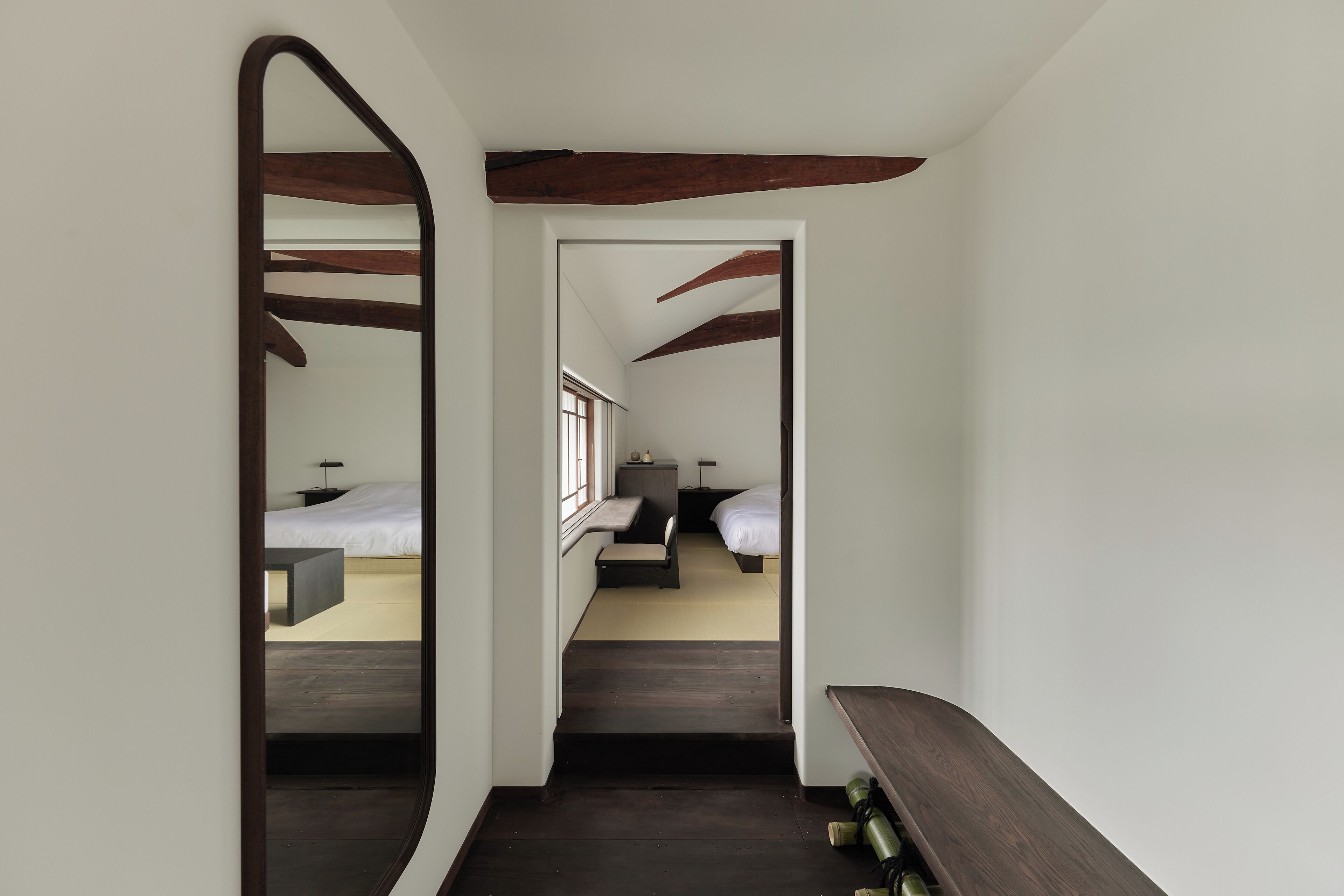 Un pasillo estrecho con vigas de madera y un banco, que conduce a un dormitorio con cama y mesita de noche.