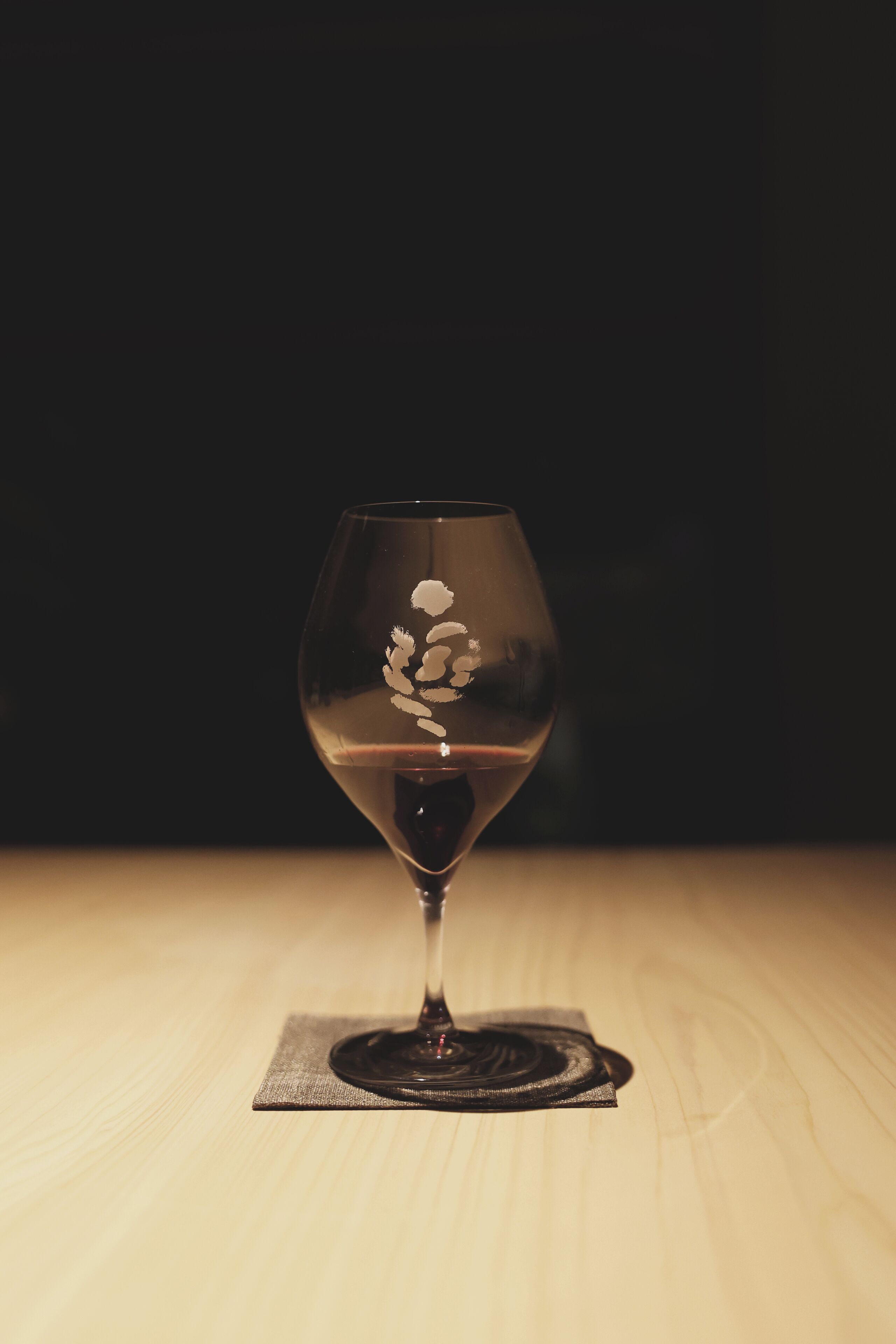 A wine glass with a floral design on a coaster, placed on a wooden surface.