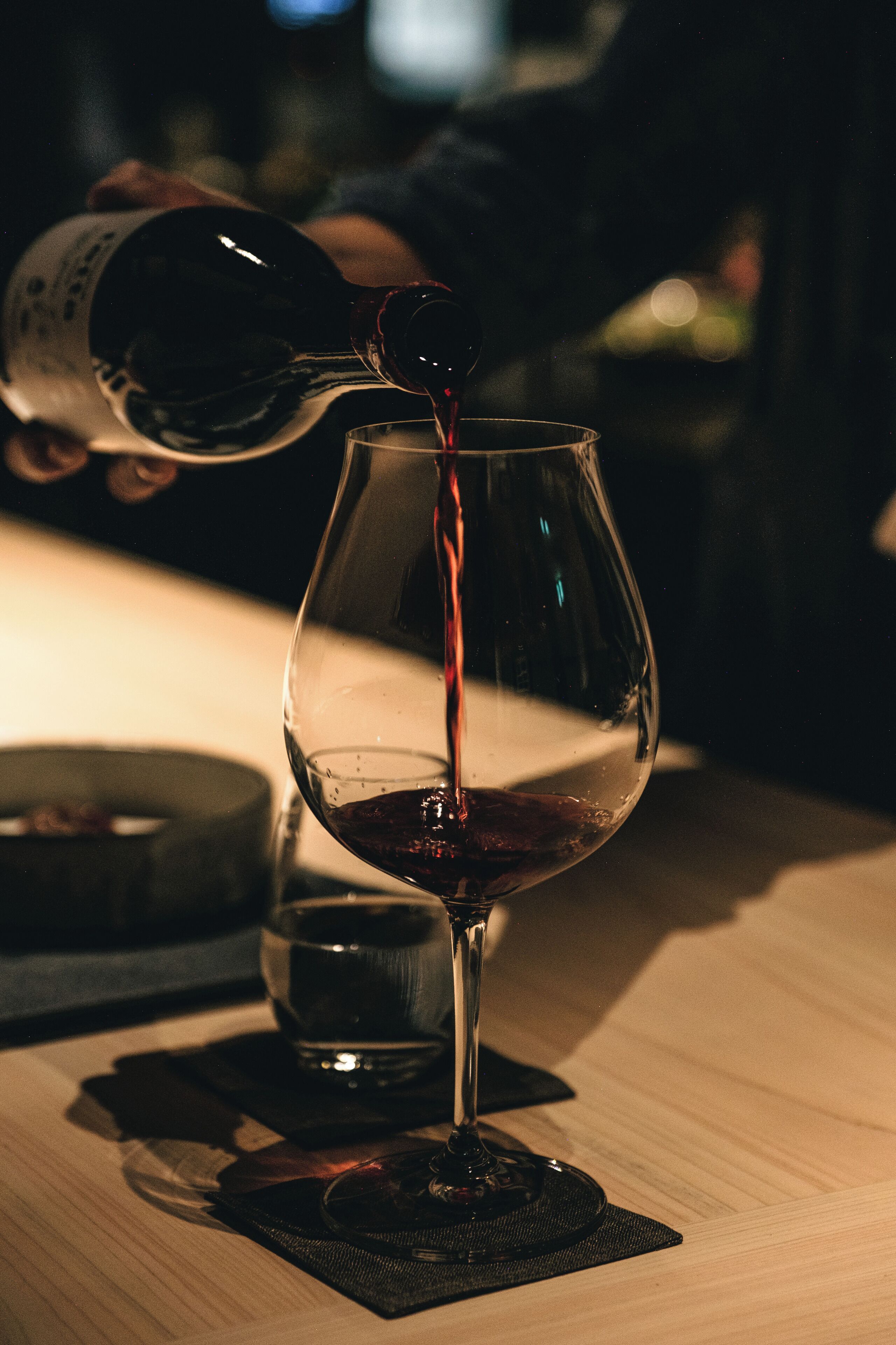 A wine glass being filled with red wine on a wooden table.