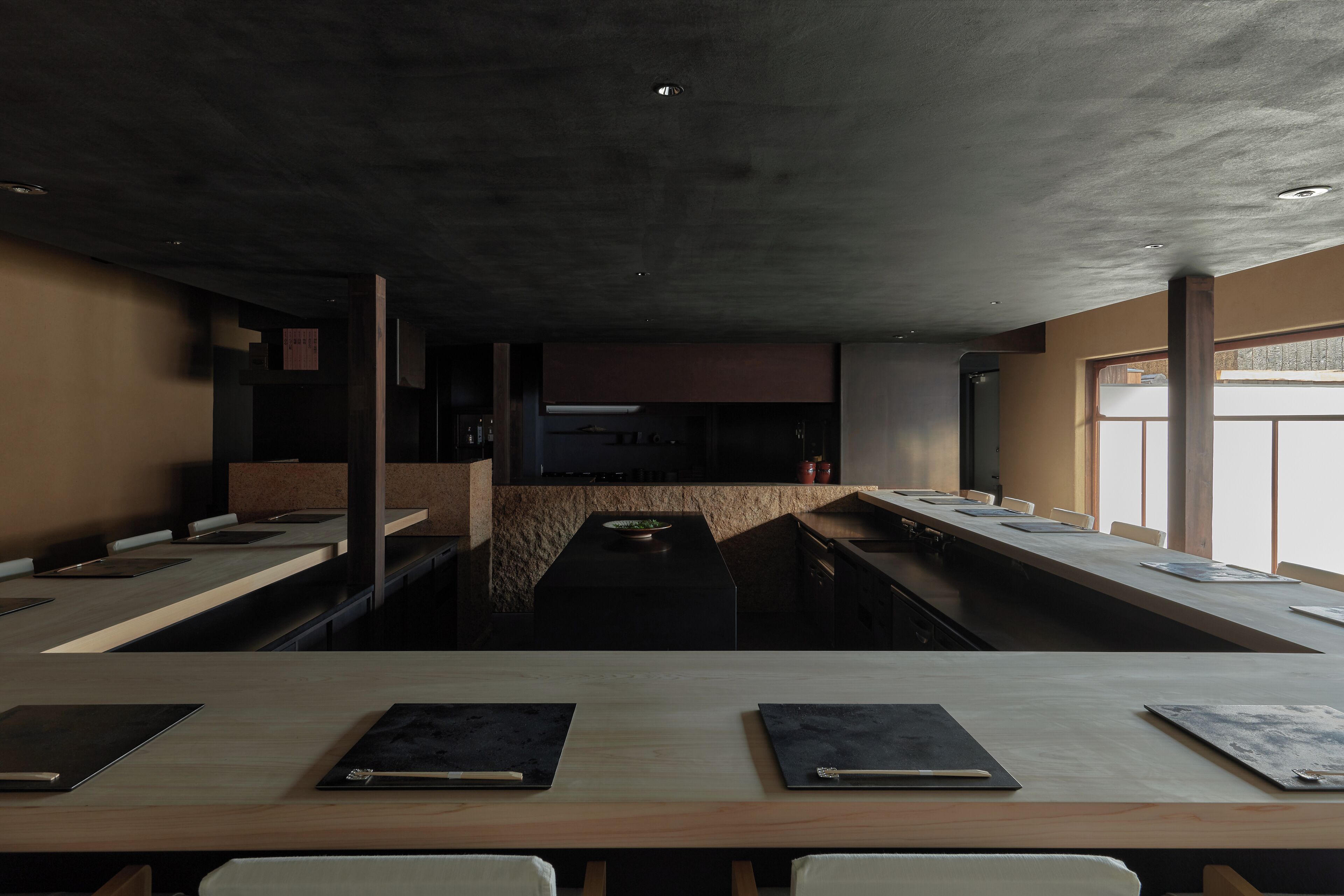 A modern conference room with a long table, chairs, and a kitchen area in the background.