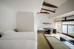 Una habitación de hotel moderna con una cama grande, una mesita pequeña y vistas al exterior a través de amplias ventanas.
