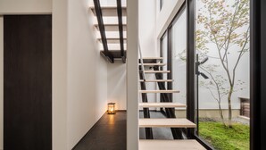 A modern interior with a staircase, a small table, and a view of a tree outside.