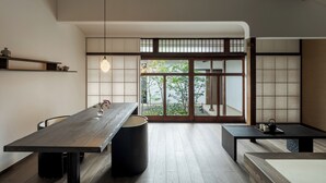 A minimalist room with a wooden table, a black trash bin, and a view of a garden through a sliding door.