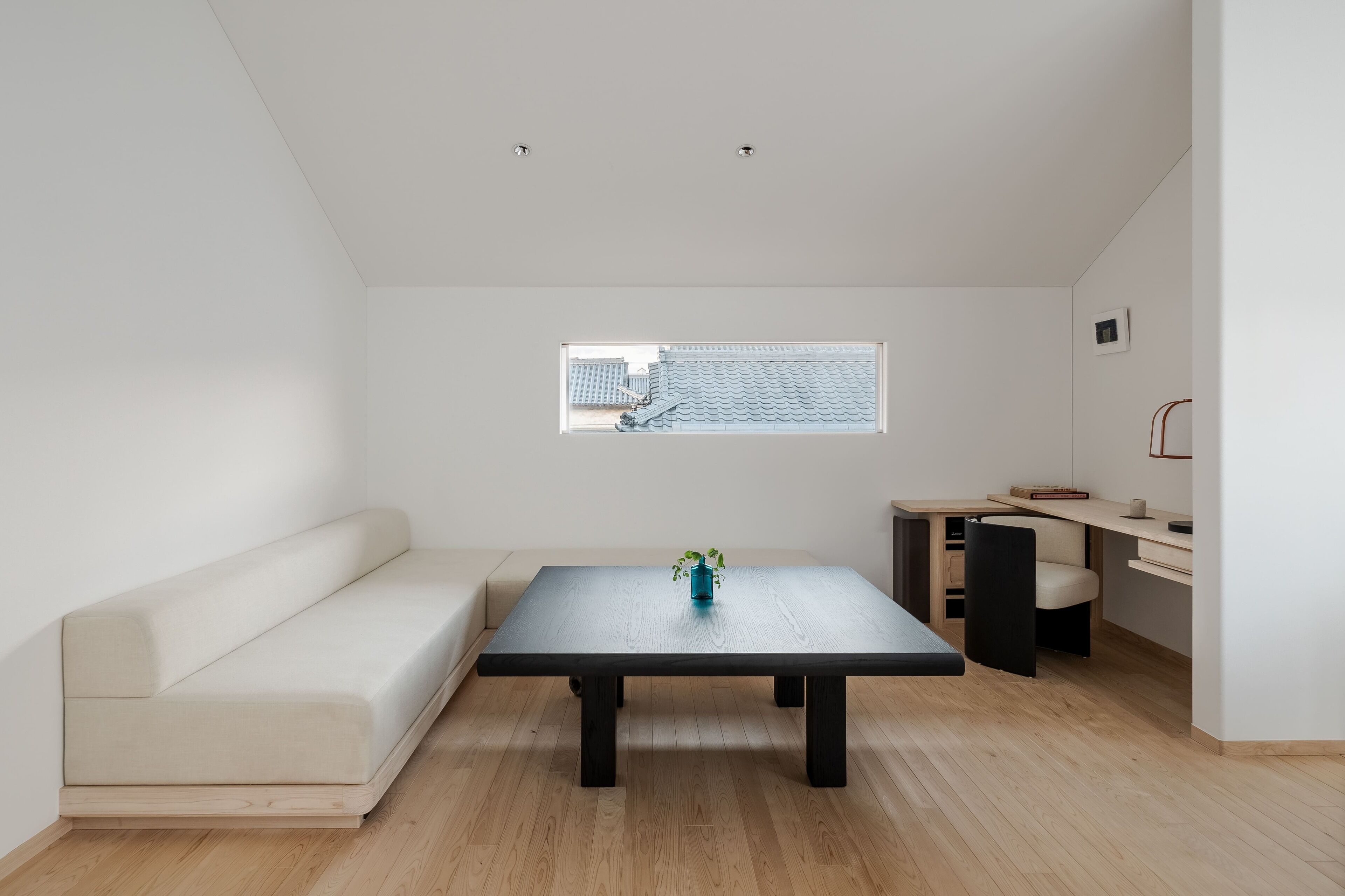 A modern, minimalist room with a sofa, a table, a small window, and a desk area.
