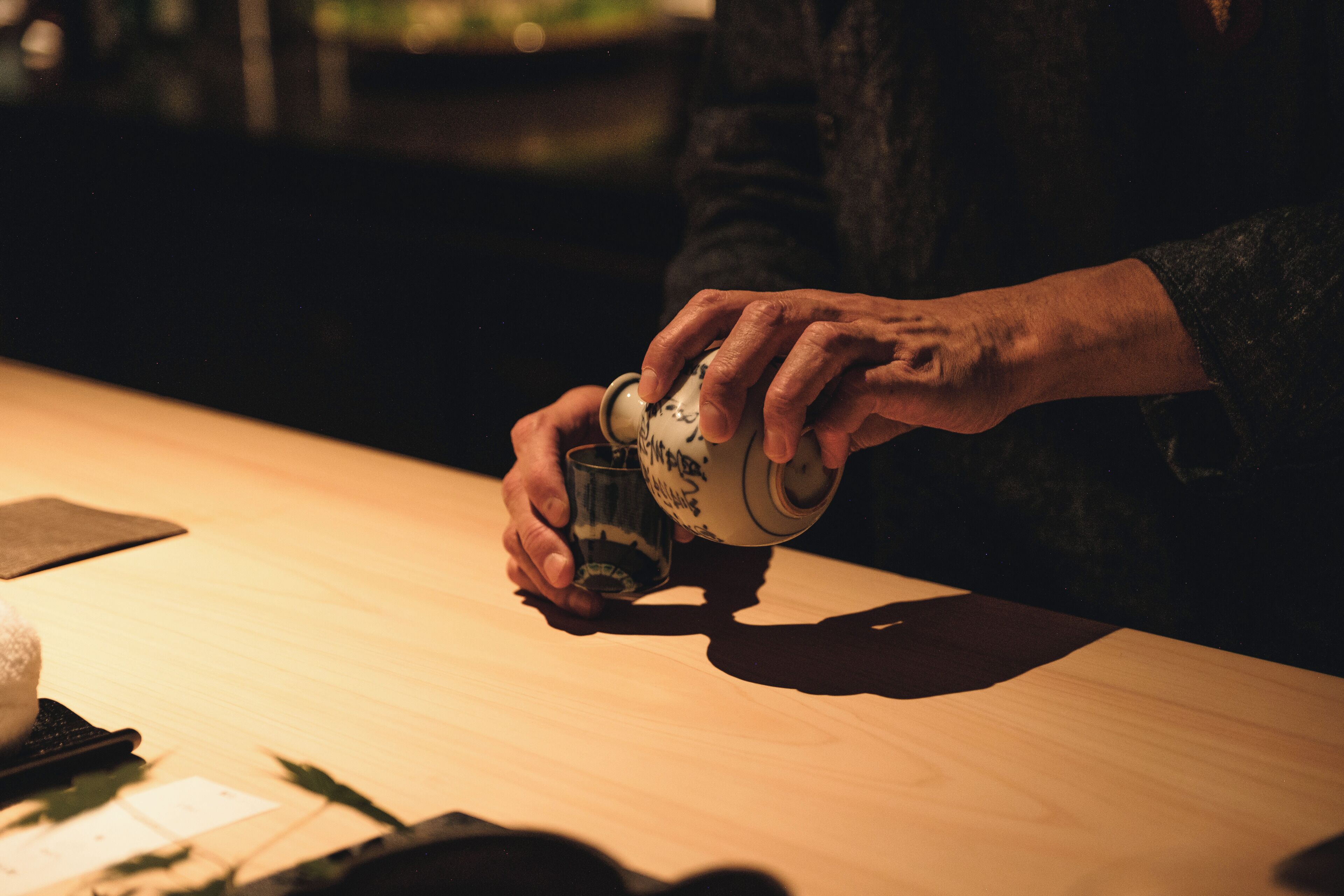Una persona sirve una bebida de una taza de cerámica sobre una mesa de madera.