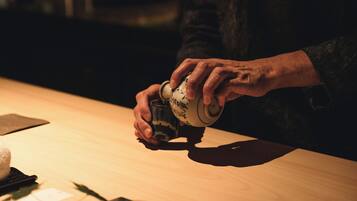 Una persona sirve una bebida de una taza de cerámica sobre una mesa de madera.
