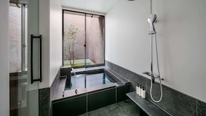 A modern bathroom with a large bathtub, a showerhead, and a window overlooking a brick wall.