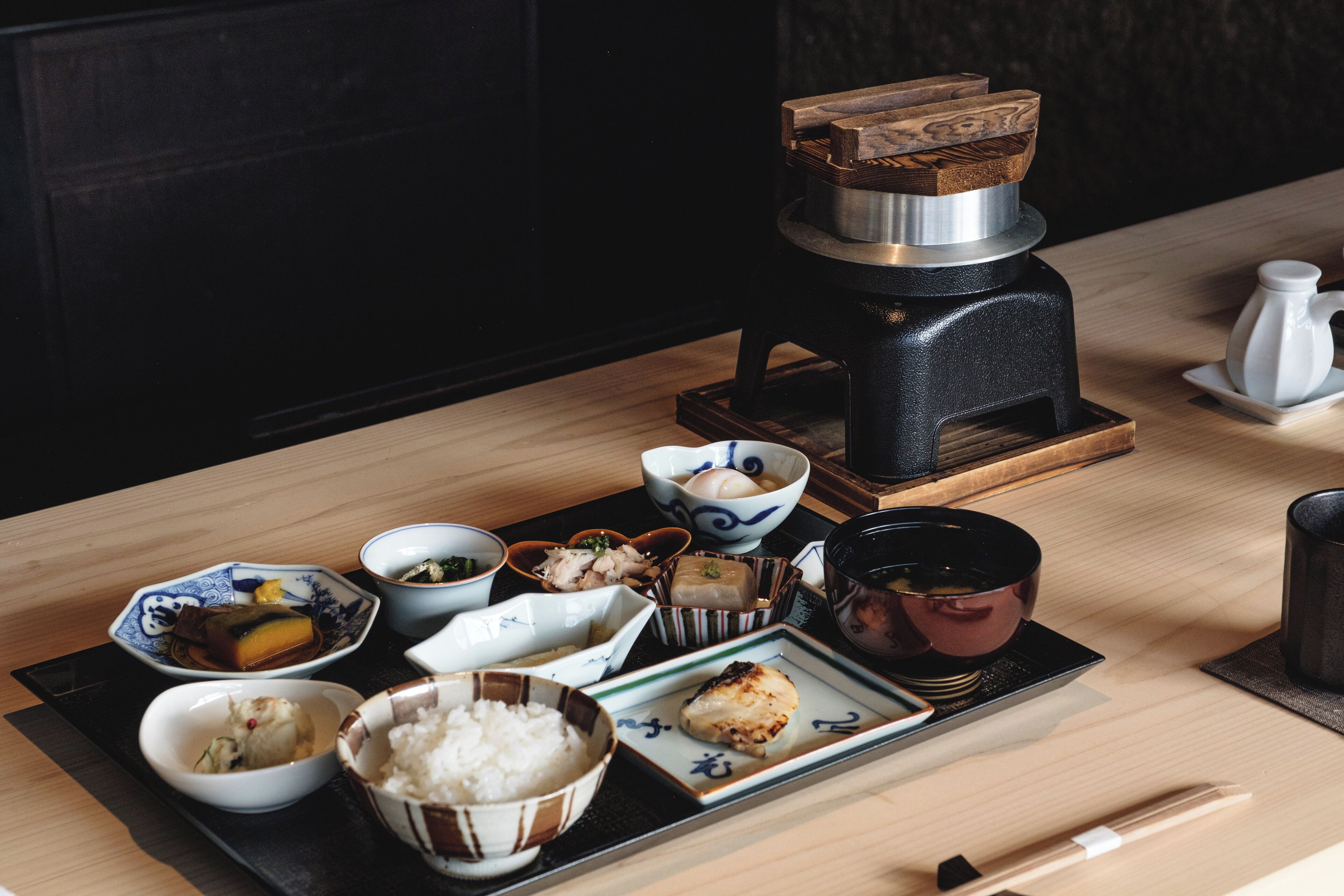 Un repas japonais traditionnel, composé de différents plats et accompagné d’une théière, est servi sur une table en bois.