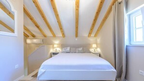A bedroom with a large bed, wooden beams on the ceiling, two bedside tables with lamps, and a window with curtains. - Cavtat Cozy Retreat Close to Beach (Konavle)