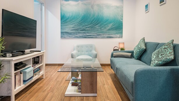 Ein Wohnzimmer mit großem Fernseher, einem Glastisch, einer Couch und einem Gemälde einer Welle.