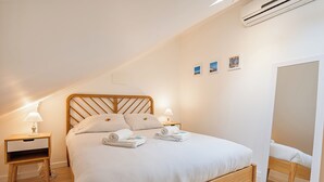 Ein ordentlich bezogenes Bett mit Holz-Kopfstuebe, zwei Nachttische mit Lampen und ein großer Spiegel an der Wand.